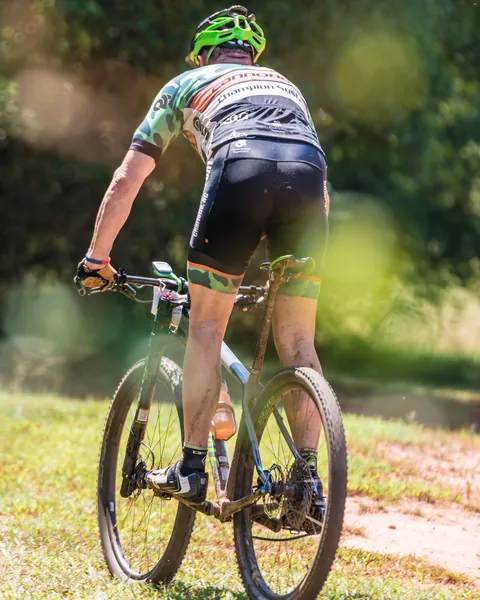 Ciclista de montaña de espaldas pedaleando por un sendero de pasto y tierra