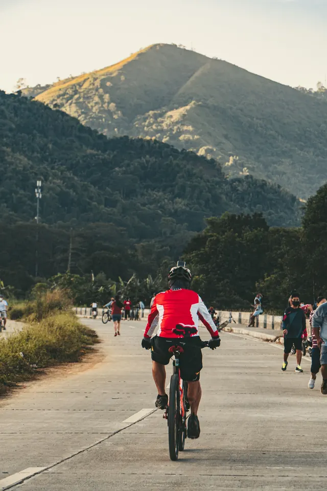 Ciclista de espaldas subiendo por una carretera con montañas al fondo
